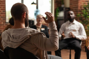 group of men and women seated in a circle discussing the 5 benefits of addiction counseling