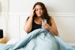 woman sitting in bed with a bad hangover with no understanding of alcohol poisoning and how it could affect her