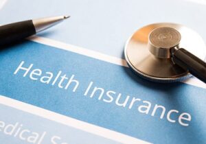a pen and stethoscope lay on top of health insurance coverage documents from aetna insurance