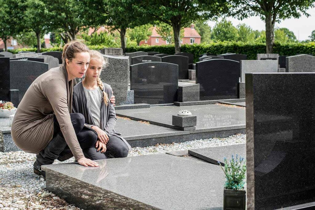 mother and her young child in a sunlit cemetery develop understanding of the opioid epidemic by visiting the grave of a loved one