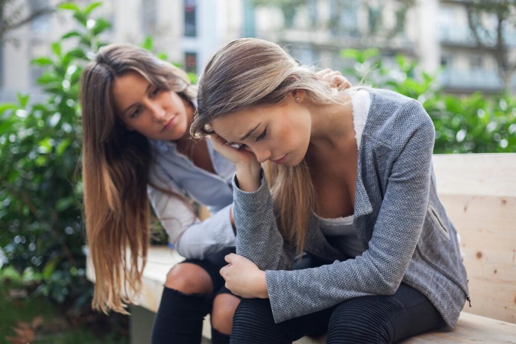young woman consoling her female friend as she explains common signs of opiate abuse and encourages her to seek help