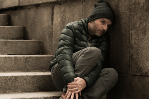 young man looking dejected and alone seated on concrete steps in outdoor stairwell exhibiting common signs of cocaine use