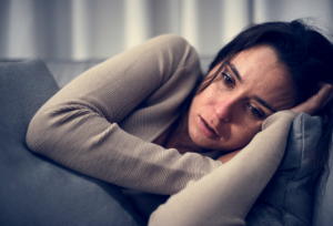 young woman looking distraught while lying on couch and wondering why are opioids addictive