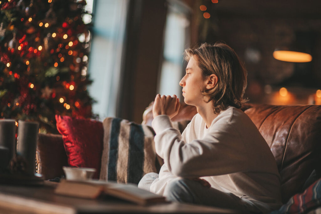 stressed-looking woman sated on couch by Christmas tree pondering the connection between holiday stress and relapse