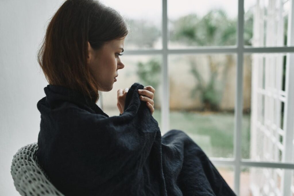 young woman seated on couch and looking uncomfortable and in pain as she struggles with opioid withdrawal symptoms