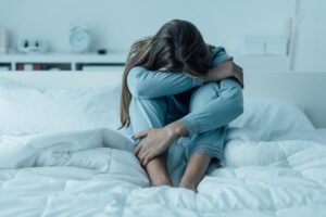 young woman curled up in fetal position on her bed struggling with trauma and addiction.