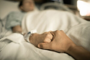 close up of a person clasping the hand of another person in a hospital bed symbolizing what to expect in a partial hospitalization program