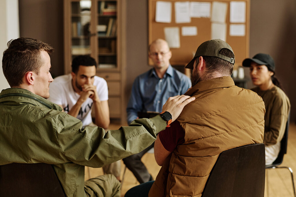 a group of adults seated in a circle with a behavioral health specialist learning what to expect in group therapy for addiction.