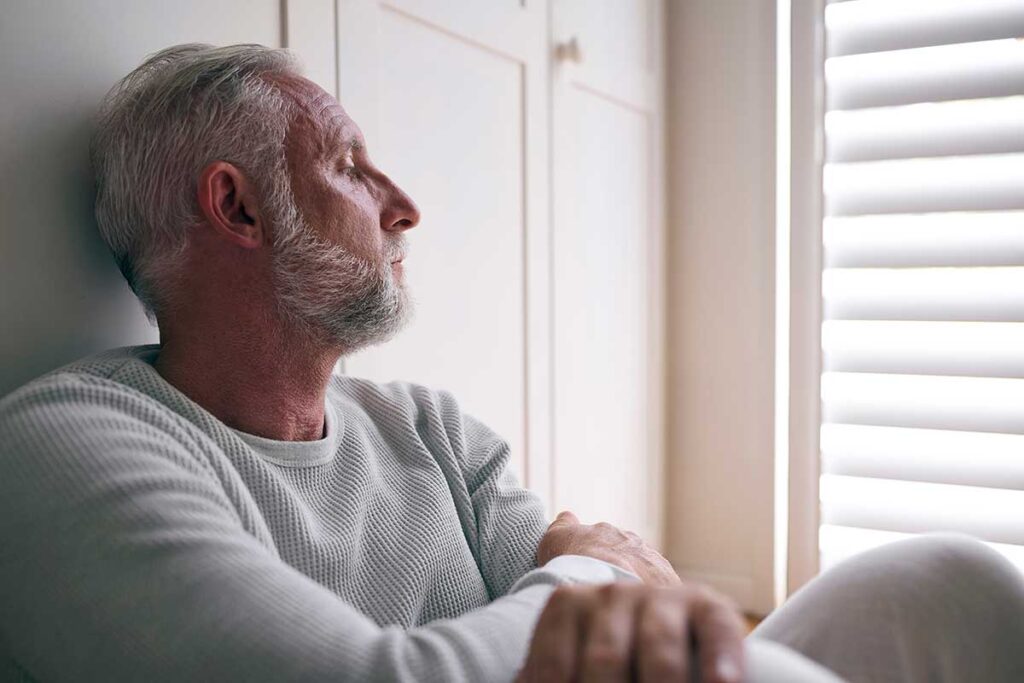 middle-aged man looking depressed as he sits in room and stares out window while suffering painkiller addiction effects, both short-term and long-term