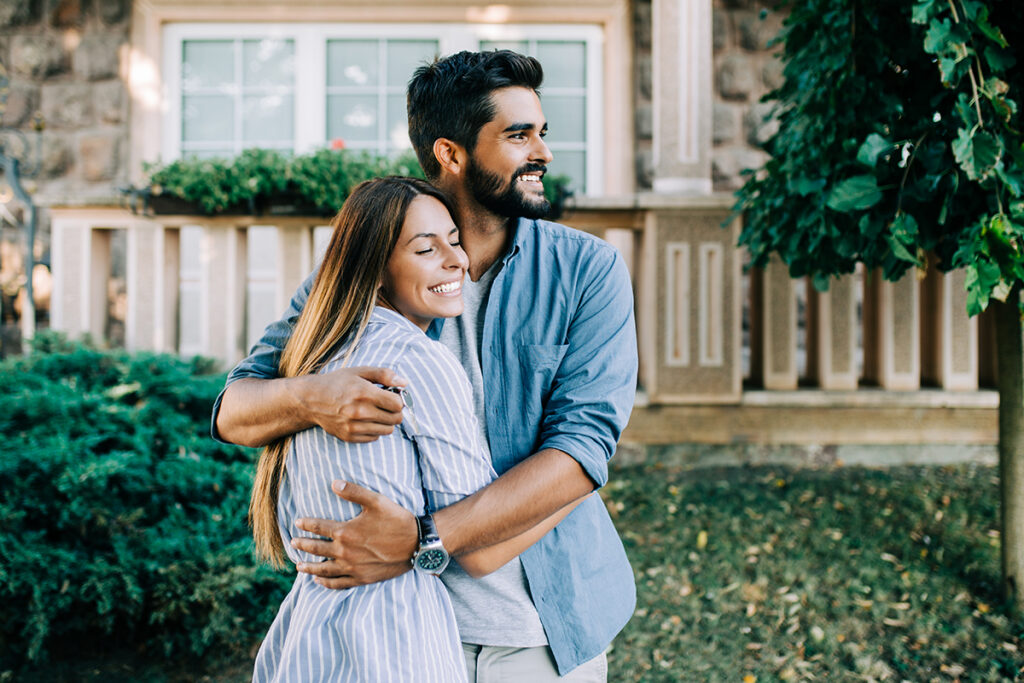 Beautiful happy young couple standing together outside in front of their new home.